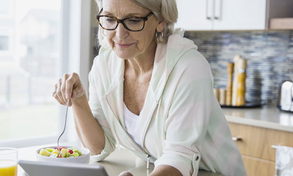 Woman wearing a pink and green sweater and eyeglasses eating a salad and looking down.