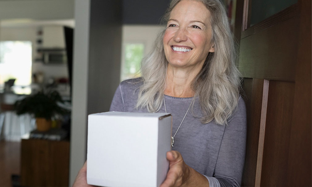 Woman wearing a grey shirt smiling and holding a white package.