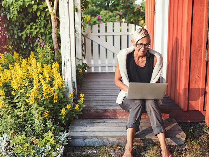 Woman sitting on a step wearing eye glasses and a black top looking at her laptop.