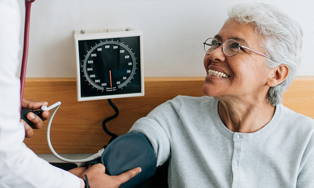 Woman wearing a grey sweater and eyeglasses smiling while having her blood pressure taken.