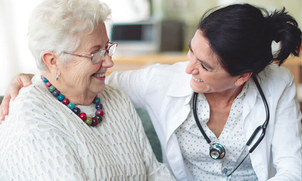 Elderly female wearing glasses and a sweater smiling with a female healthcare provider.