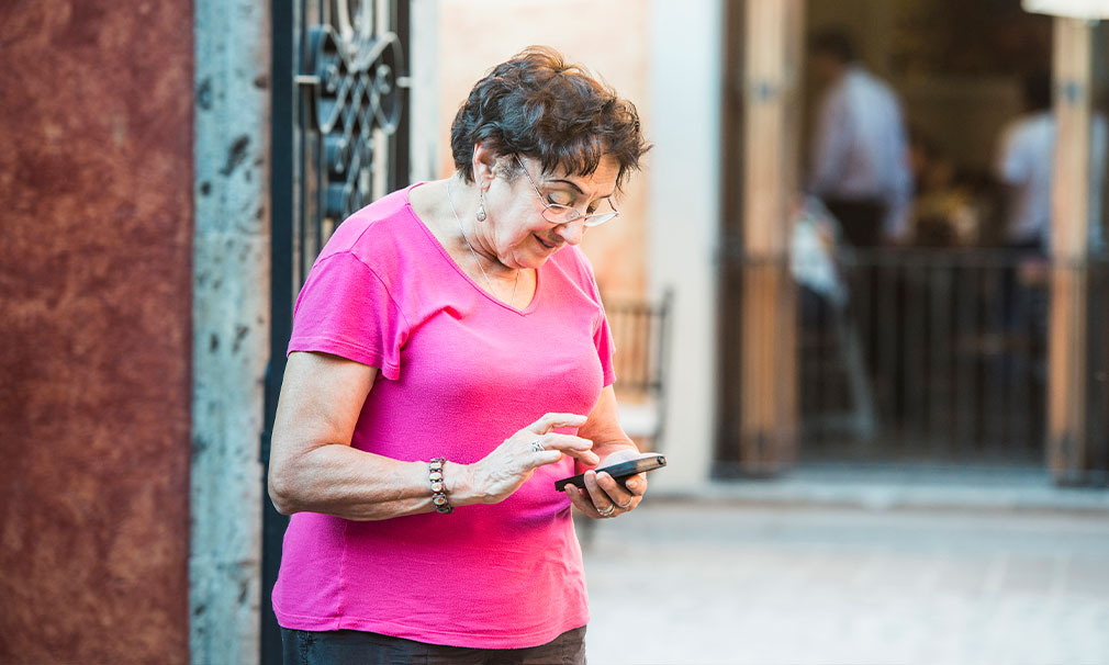 Woman wearing eyeglasses and a pink shirt looking down at her phone and typing.